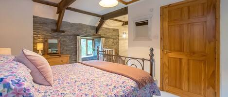 A bedroom with a bed, a wooden door, and a stone wall.