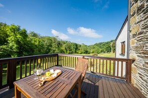 A wooden deck with a table set for a meal, overlooking a green landscape. - One Bedroom Barn Conversion near Aberteifi | Certws-Y-Rhiw (Penparc)