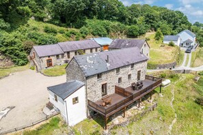 A stone building with a deck, surrounded by a gravel driveway and lush greenery. - One Bedroom Barn Conversion near Aberteifi | Certws-Y-Rhiw (Penparc)