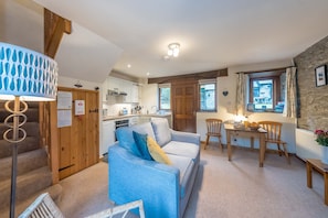 A cozy living room with a sofa, a dining table with chairs, a kitchen area, and a staircase. - One Bedroom Barn Conversion near Aberteifi | Certws-Y-Rhiw (Penparc)