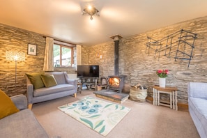 A cozy living room with a stone wall, a fireplace, a television, and a sofa. - A Converted Barn in a Beautiful Valley in Ceredigion | Granar-Y-Rhiw (Cardigan)