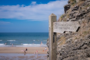 A wooden signpost with text, a beach, and the ocean in the background. - A Converted Barn in a Beautiful Valley in Ceredigion | Granar-Y-Rhiw (Cardigan)