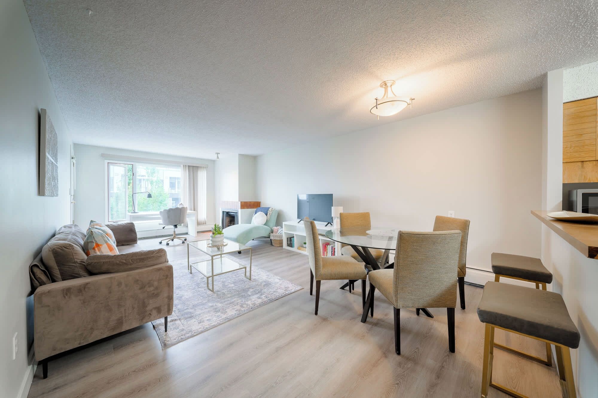 Een moderne woonkamer met een bank, salontafel en stoelen. Er is een open haard, een televisie en een eethoek met een tafel en stoelen.