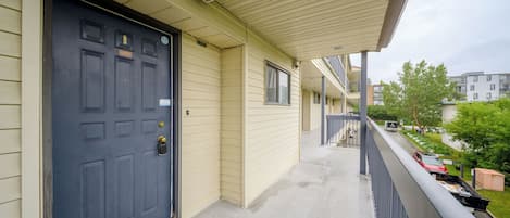 A residential building with a dark blue door, a covered balcony, and a view of a parking area with cars and greenery.
