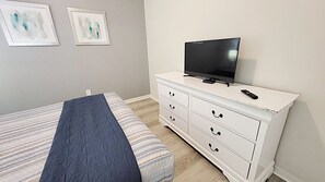 Ein Schlafzimmer mit einem Bett, einer Kommode mit Fernseher und zwei gerahmten Bildern an der Wand.
