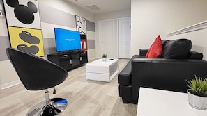 Ein modernes Wohnzimmer mit einem schwarzen Sofa, einem weißen Couchtisch, einem schwarzen Sessel und einem Flachbildfernseher.