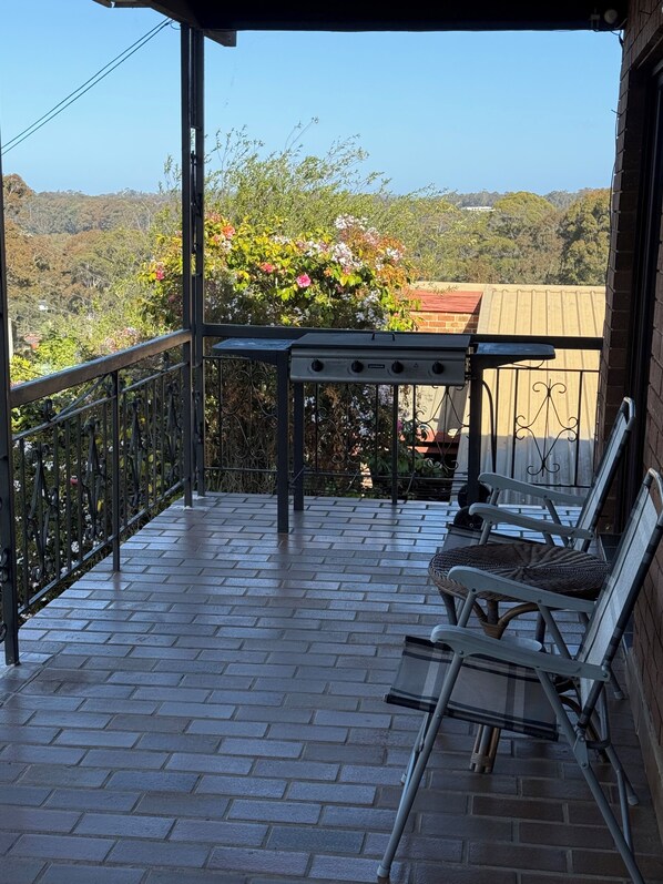 A balcony with a brick floor, metal railing, and a table with chairs.