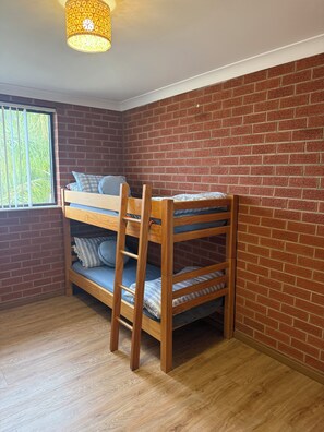 A bunk bed with a wooden frame and blue bedding, a brick wall, and a window with bars.