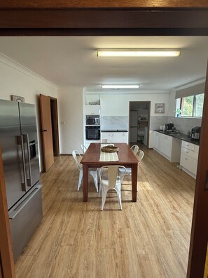 A modern kitchen with a wooden dining table, white chairs, and built-in appliances. - The Lion’s Gate - family friendly 3-bedroom house moments from the beach (Catalina)
