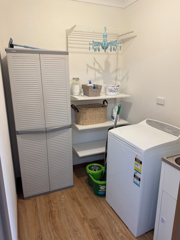 A laundry room with a washing machine, a dryer, shelves with baskets, and a mop.