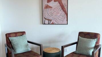 Deux fauteuils recouverts d’un tissu à motifs, un tabouret en osier et une œuvre d’art encadrée accrochée au mur.