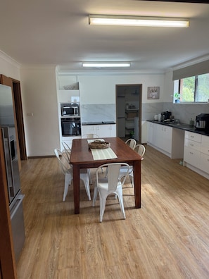 A modern kitchen with white cabinetry, a wooden dining table, and a built-in oven.