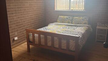 Une chambre avec un lit en bois, un mur en briques, une fenêtre avec des stores et une petite table de chevet.