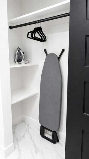 Ein Kleiderschrank mit Kleiderstange, Bügelbrett und Bügeleisen.