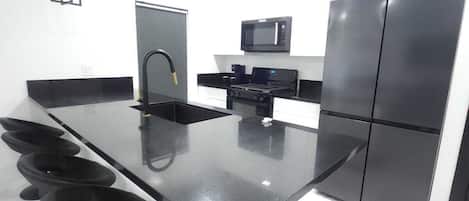 Una cocina moderna con una isla central, electrodomésticos negros y encimera de mármol blanco.