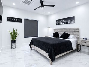 Ein modernes Schlafzimmer mit einem Bett, einem Nachttisch, einer Wanduhr, einem Deckenventilator, einem Fenster mit Jalousien und einem Stadtbild.