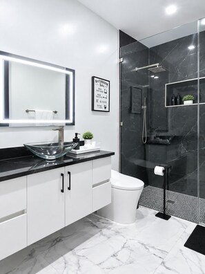 Een moderne badkamer met een glazen douchecabine, een wit toilet en een zwart aanrecht met een wastafel van glas.