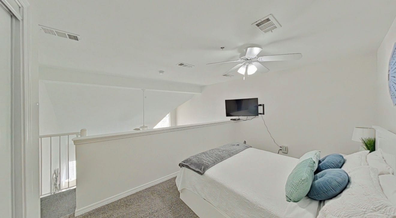 A bedroom with a bed, pillows, a ceiling fan, a mounted TV, and a window.