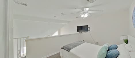 Un dormitorio con cama, almohadas, ventilador de techo, televisor montado y ventana.