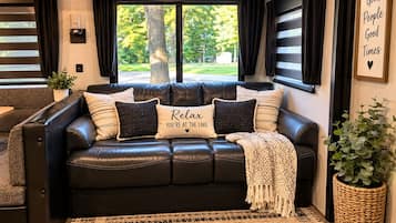 Un sofá de cuero negro con varios cojines, una alfombra tejida y un cartel enmarcado en la pared.