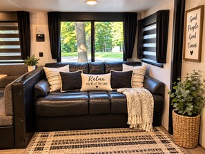 En svart lädersoffa med flera kuddar, en vävd matta och en inramad tavla på väggen.