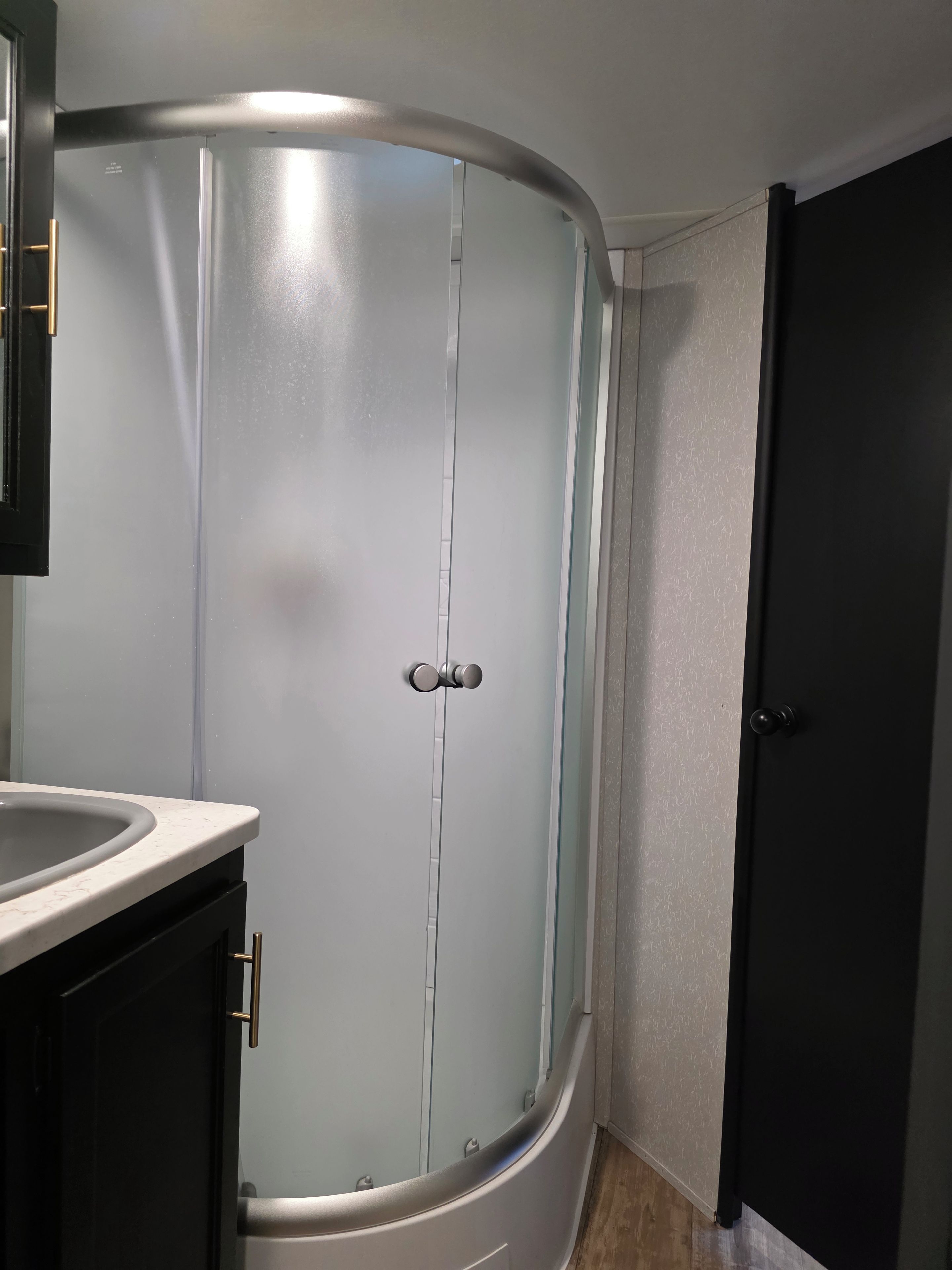 Un baño con cabina de ducha curva, un lavabo y una puerta oscura.