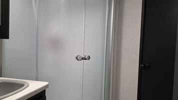 Un baño con cabina de ducha curva, un lavabo y una puerta oscura.