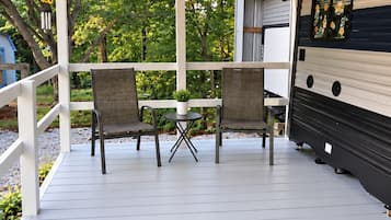 En takförsedd uteplats med två stolar och ett bord, en takfläkt och en husbil i bakgrunden.