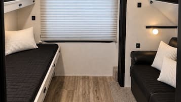Ett kompakt inre utrymme i husbilen med en TV monterad ovanför ett fönster, två våningssängar och en liten sittgrupp.