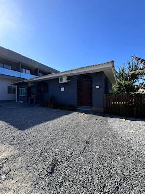 A building with a gravel driveway, a wooden fence, and a clear blue sky. - Joaquina's Retreat Residences #4 (Lagoa da Conceição)