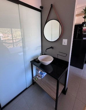 A modern bathroom with a white sink, a round mirror, and a black countertop. - Joaquina's Retreat Residences #4 (Lagoa da Conceição)