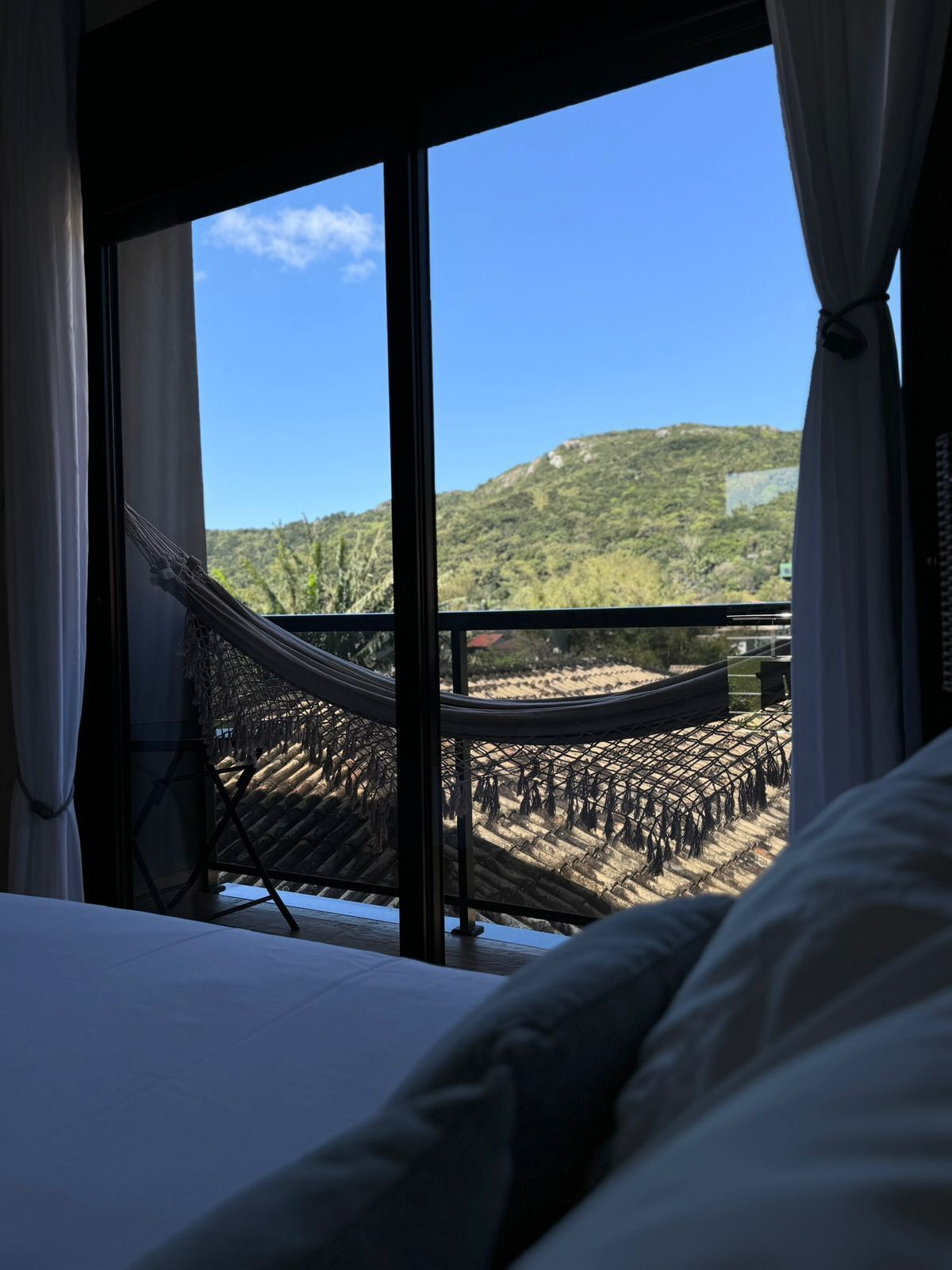 Una habitación con un ventanal grande, una hamaca y vistas a un paisaje montañoso.