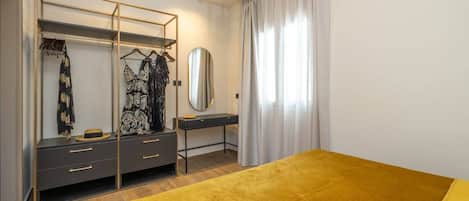 A bedroom with a bed, a wardrobe, a vanity with a mirror, and a window with curtains.