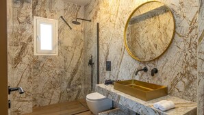 Kylpyhuone, jossa on marmoriseinä, kultainen pesuallas, wc ja suihkutila.