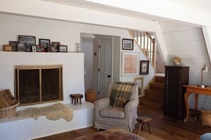 Uma sala de estar acolhedora com lareira, uma poltrona listrada, uma escada de madeira e uma coleção de quadros na parede.