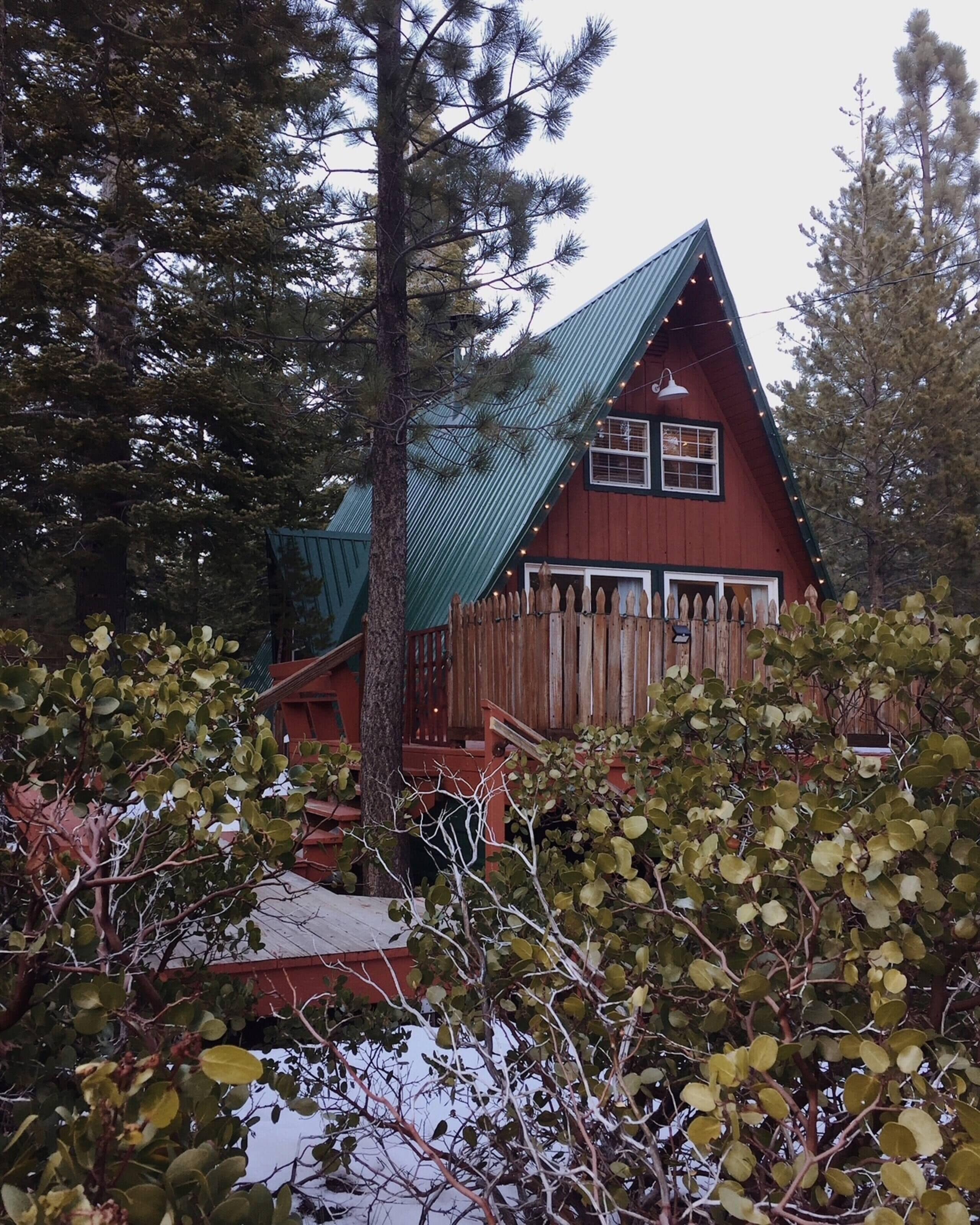 A cabin with a steeply pitched roof, wooden deck, and a fenced yard.