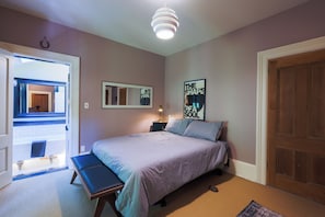 A bedroom with a bed, a bench, a bedside table, a mirror, and a door. - The Victorian Garden Retreat (Victoria)