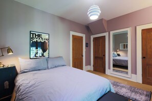 A bedroom with a bed, a bedside lamp, a poster on the wall, and a door leading to another room. - The Victorian Garden Retreat (Victoria)