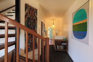 A hallway with a wooden staircase, a patterned rug, a bookshelf, and a large abstract painting. - The Victorian Garden Retreat (Victoria)
