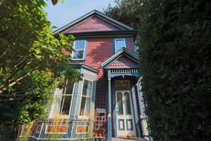 A two-story house with a red exterior, a bay window, and a front door with a number plaque. - The Victorian Garden Retreat (Victoria)