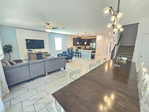 A modern living room with a grey sofa, a dining area with a dark wooden table, and a kitchen with dark cabinets and stainless steel appliances. - 9BR ChampionsGate Villa | Private Pool & Spa | Game Room | Near Disney (Davenport)