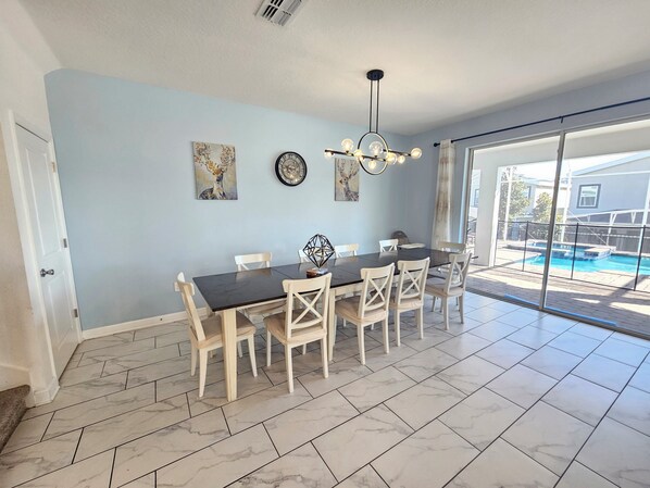 A dining area with a table and chairs, a ceiling light, and a view of a swimming pool through large glass doors. - Marvelous 9-bedroom house with AC in peaceful Davenport (Davenport)