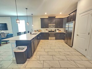 A modern kitchen with dark cabinets, a central island, stainless steel appliances, and pendant lighting. - 9BR ChampionsGate Villa | Private Pool & Spa | Game Room | Near Disney (Davenport)