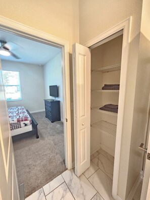 Une chambre à coucher comprenant un lit, une commode, un téléviseur et un placard avec des étagères.