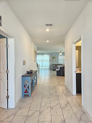 A hallway with a kitchen area in the background, featuring a dining table and chairs, and a tiled floor. - 9BR ChampionsGate Villa | Private Pool & Spa | Game Room | Near Disney (Davenport)