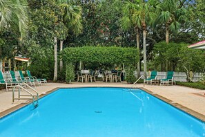 Ein Schwimmbecken mit Liegestühlen und Tischen, umgeben von Bäumen und einem weißen Zaun.