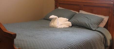 A bed with a blue bedspread and pillows, a wooden headboard, and a wooden nightstand.