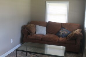A living room with a brown sofa, two patterned pillows, and a glass coffee table. - Cozy Mountain Home (East Flat Rock)