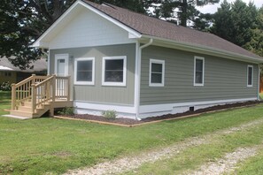 A single-story house with a front porch, a small front yard, and a gravel driveway. - Cozy Mountain Home (East Flat Rock)