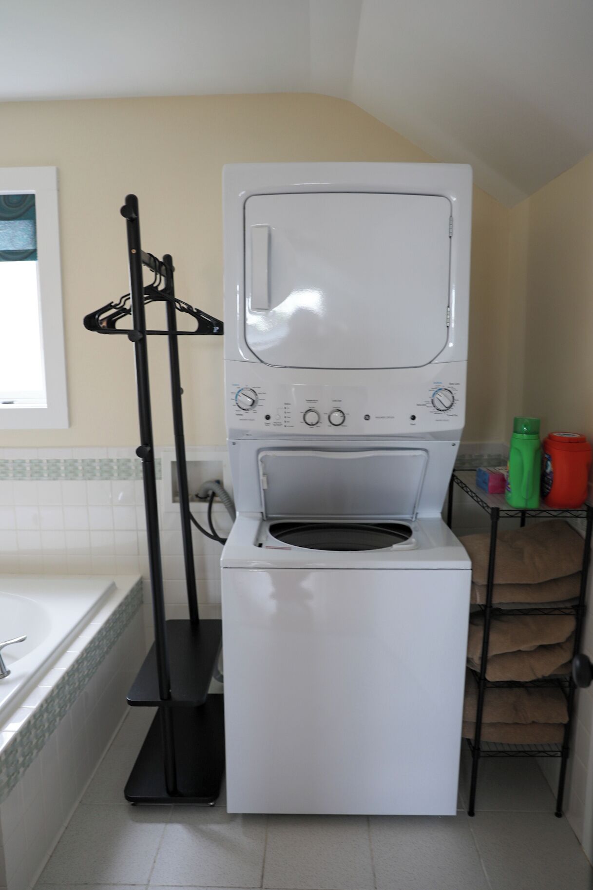 Un espace buanderie compact comprenant un lave-linge et un sèche-linge, un étendoir et une petite étagère avec des produits de nettoyage.